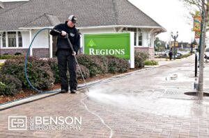 A worker uses a pressure washer to clean a sidewalk in front of a Regions bank building.