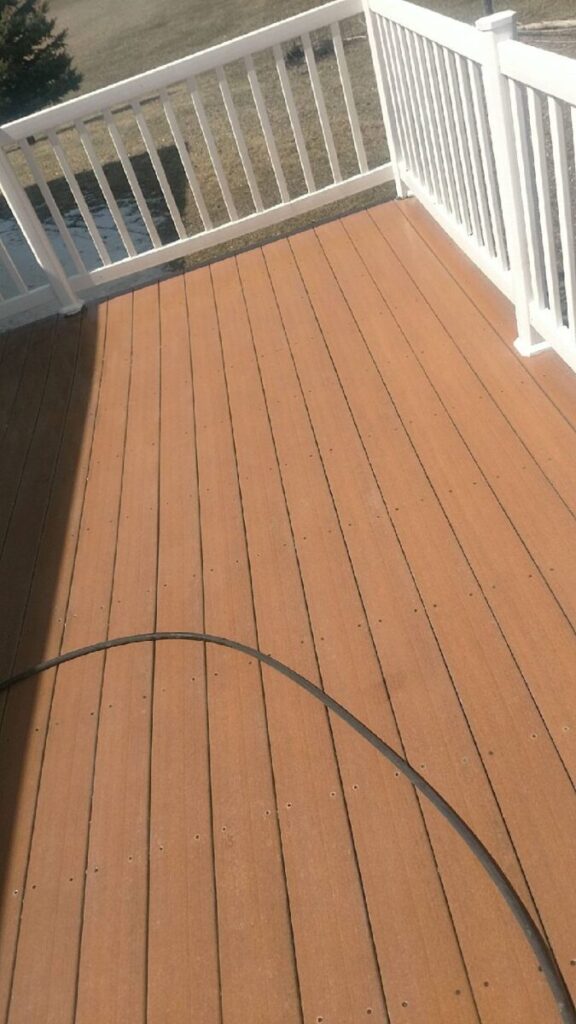 A brown wooden deck with white railings and a black hose lying across the floor, in outdoor daylight.