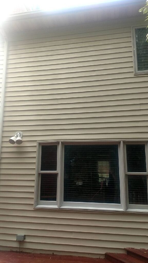The exterior wall of a house with beige vinyl siding, three windows, and an outdoor light fixture above.